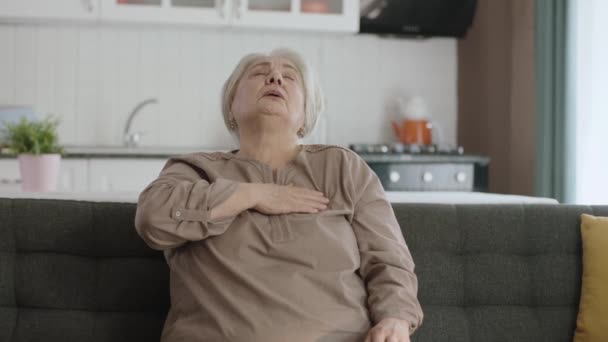 胸に痛みを感じるお年寄り家庭の椅子に座っているお年寄りの女性が心臓発作を起こしています 心臓の動悸を持つ老婦人の肖像画 急性胸痛心臓発作 — ストック動画