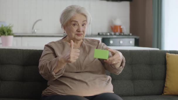 Anciana Sostiene Algo Verde Sillón Mostrando Producto Sonriendo Presentando Objeto — Vídeos de Stock