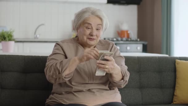 快乐的老妇人对她的钱很满意 赢得网上抽奖 快乐的老年妇女持有很多美元 兴奋的老妇人一个人在家享受她的钱 — 图库视频影像