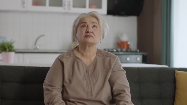 老妇人指着上面的广告空间 看这里 快乐的老妇人坐在沙发上 仰头看信息 展示出头顶上的复制空间 — 图库视频影像