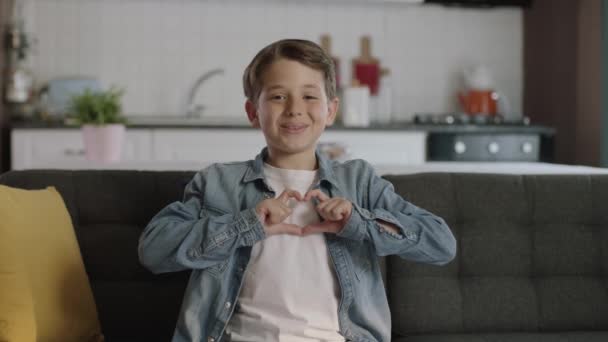 Kanepede Oturan Sevimli Küçük Çocuk Kameraya Elleriyle Kalp Şekli Veriyor — Stok video