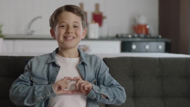 Cute Little Boy Siedzi Kanapie Dając Kształt Serca Aparatu Rękami — Wideo stockowe