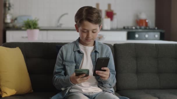Технология Дополняет Маленького Мальчика Сидящего Диване Играющего Игры Двумя Смартфонами — стоковое видео
