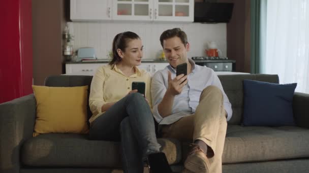 Ευτυχισμένο Ζευγάρι Μιλάμε Γελώντας Στον Καναπέ Κοιτάζοντας Smartphone Χρησιμοποιώντας Apps — Αρχείο Βίντεο