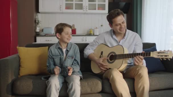 Otec Hraje Kytaru Svému Synovi Zatímco Sedí Doma Pohovce Mladý — Stock video