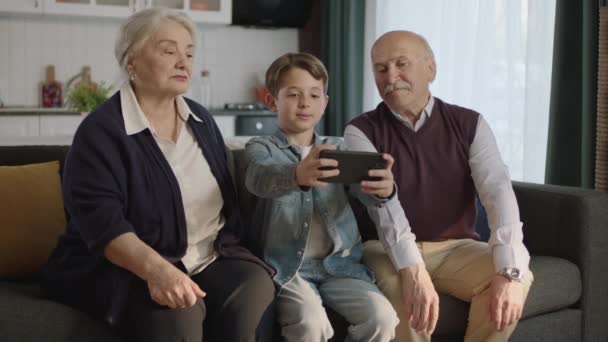 Mały Chłopiec Odwiedza Dziadków Szczęśliwa Para Starców Siedzi Kanapie Rozmawia — Wideo stockowe