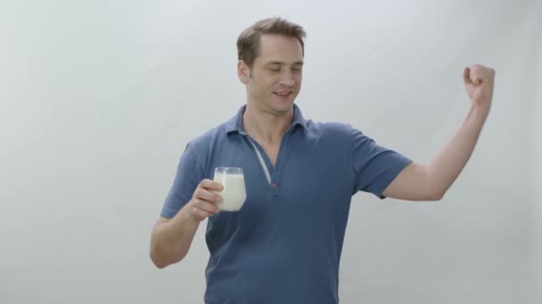 白い背景にミルクのガラスの若い男 男は牛乳を飲み 彼の両足を示す 健康だ カルシウムの力 白い背景にミルクを飲んだ後に二足歩行を示す若い男 — ストック動画