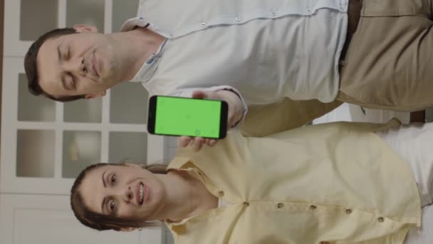 キッチンのダイニングテーブルでスマートフォンを使用して幸せなカップル 銀行口座をチェックし オンラインショッピング ソーシャルネットワークをチェックし レストランから食べ物を注文します 彼らはカメラに緑色の画面電話を示しています 垂直ビデオ — ストック動画