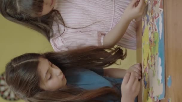 两个漂亮的姐姐或朋友在家里做拼图 孩子们互相学习如何解谜 两个小女孩一起坐在桌旁解谜 — 图库视频影像