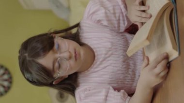 Uzun saçlı küçük bir kız odasında bir kitap okuyor. Sevimli küçük kız kitap okuyor, sayfayı çeviriyor, öğreniyor, çalışıyor, çalışıyor, kitap okuyor..