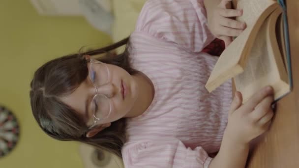 長い髪の少女が部屋で本を読んでいる かわいい女の子は本を読んで ページをめくり 勉強し 本を読む垂直ビデオ — ストック動画