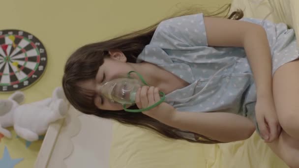 小さな女の子は 子供のベッドで息の不足している煙薬を吸入します 呼吸しようとしている呼吸器 マスクされたNebulizerと酸素マスクを使用して魔法の女の子 垂直ビデオ — ストック動画