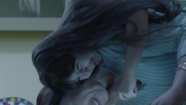 小女孩拥抱着她微笑的母亲 漂亮的年轻妈妈和她穿着睡衣的可爱女儿坐在床上 笑着看着数码平板电脑 快乐的家庭在床上冲浪 垂直视频 — 图库视频影像