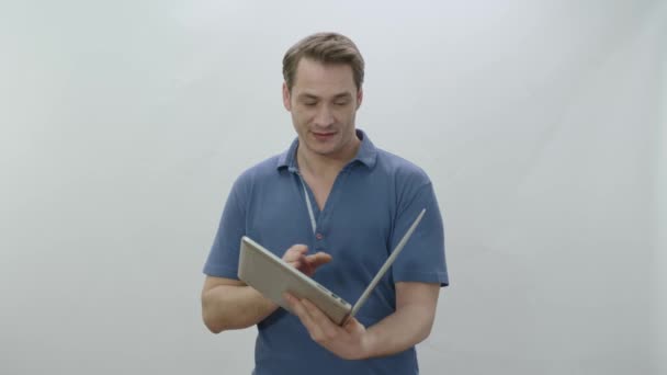 白い背景に隔離された本のようにノートパソコンを持っている男 若い男は 彼が見ているものに驚いて ノートパソコン上の本を読んでいるかのようにページを変更します 将来の技術 — ストック動画