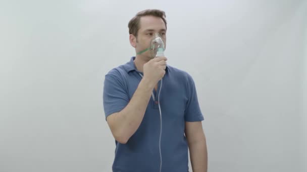 拿着蒙面雾化器的年轻人把烟雾药吸入他的午餐 生病的男人带着呼吸面罩呼吸 隔离在白色背景中 疾病概念 — 图库视频影像