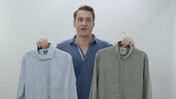 Hombre Joven Aislado Delante Fondo Blanco Sosteniendo Dos Camisas Hombre — Vídeo de stock