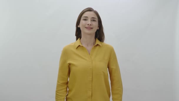 女人笑着看着白色背景上的相机 穿着黄色衬衫的漂亮女人的画像 — 图库视频影像