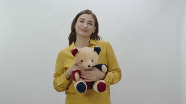 女人把泰迪熊抱在怀里 孤零零地躺在白色的背景上 可爱的年轻女人抱着一只毛茸茸的泰迪熊 礼物的概念 — 图库视频影像