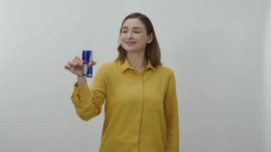 Enerji içen genç bir kadının portresi konserve kutusundan Red Bull içiyor. Mutlu genç kadın beyaz arka planda izole edilmiş favori Red Bull 'uyla serinliyor..