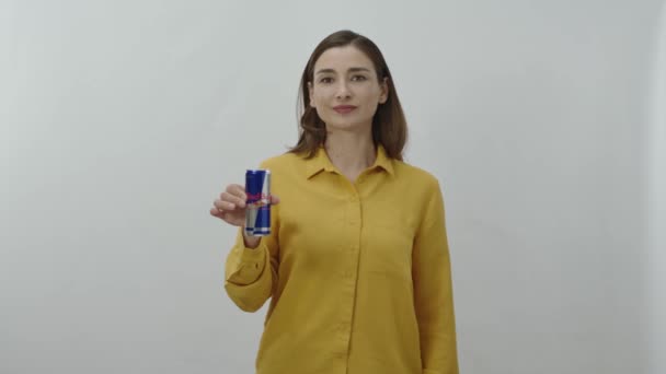 一个喝能量的年轻女人的人物肖像用铁罐喝红牛 快乐的年轻女子带着她最喜欢的红牛躲在白色的背景下 — 图库视频影像