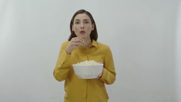 在看一部令人兴奋的电影时贪婪地吃爆米花的年轻女子的人物肖像 年轻女子在白背景下吃薯片 零食或爆米花 — 图库视频影像