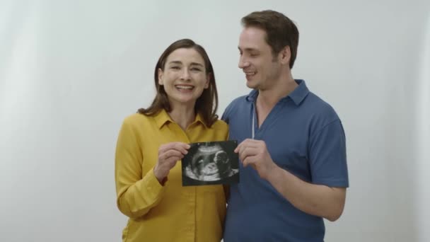 一对年轻夫妇即将生下新的孩子 因白人背景而被隔离 年轻快乐的夫妇非常相爱对方与婴儿超声照片在他们的手中 结婚周年的概念 — 图库视频影像