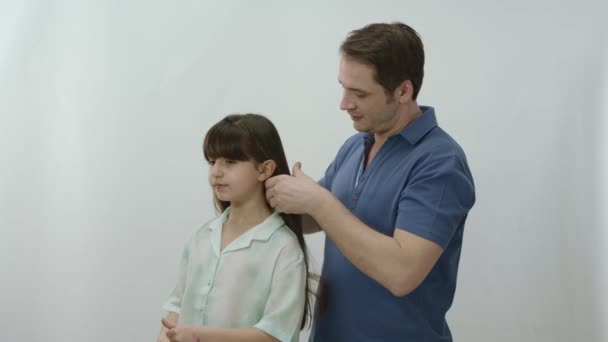 白い背景をした若い父親が娘の髪を持っている 娘を非常に愛し 学校のために彼女を準備している父は 彼女の髪を持っています 理想的な娘の肖像画 — ストック動画