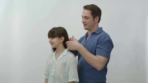 一个有着白色背景的年轻父亲正在梳理他女儿的头发 这位父亲非常爱他的女儿 为她上学做准备 正在给她梳头 理想的父亲女儿肖像 — 图库视频影像