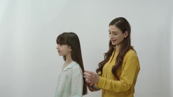 一位有着白色背景的年轻母亲正在梳理女儿的头发 这位非常爱女儿 为女儿上学做准备的母亲正在梳理她的头发 — 图库视频影像