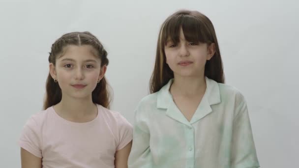 两个漂亮的小女孩在白色背景上的画像 可爱的小女孩笑着看着白色背景的相机 — 图库视频影像