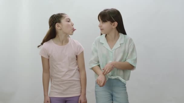 白い背景に二人の少女が互いに舌を突き出している 互いに愛し合い 話し合いをしない人たち 女の子たちはお互いに — ストック動画