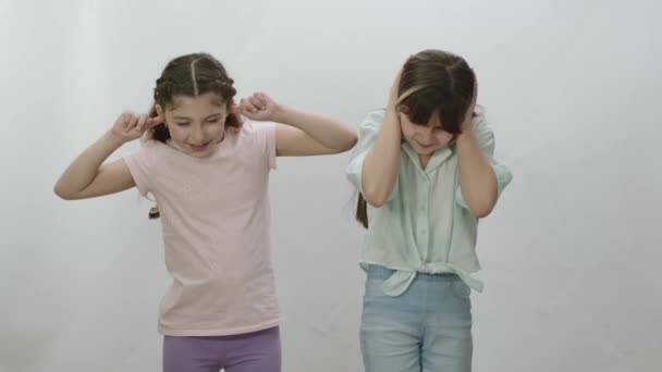 白い背景の上にお互いの隣に立っている2人の女の子 カジュアルな服の小さな無力女の子は大声で叫び 彼らの手で耳をカバー — ストック動画