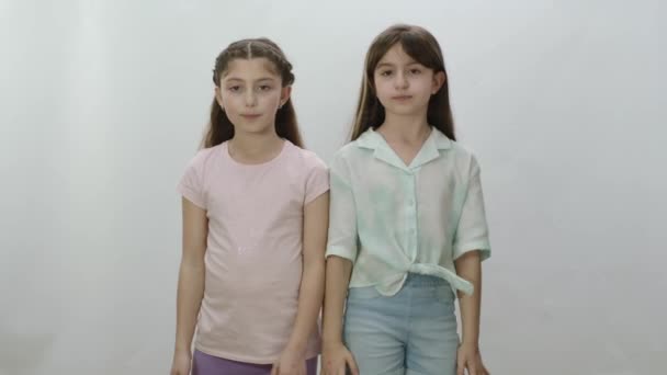 白い背景に二人の少女が並んで立っている カジュアルなTシャツやジーンズの精力的な女の子は行動を起こす準備ができてきています チームワークのコンセプト — ストック動画