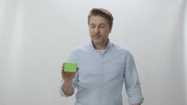 被白色背景隔离的年轻人的工作室肖像 男人拿着绿色盒子显示产品很好 创意3D艺术家可以用他们想要的任何产品替换绿色盒子 — 图库视频影像