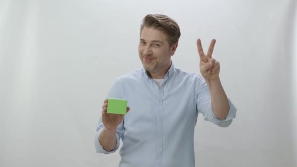 被白色背景隔离的年轻人的工作室肖像 男人拿着绿色盒子显示产品很好 创意3D艺术家可以用他们想要的任何产品替换绿色盒子 — 图库视频影像