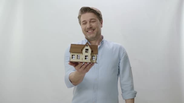 分析是否购买或投资于房屋或房地产 快乐的年轻人正在研究他在白色背景下购买或租赁的新房子的蓝图模型 新建筑项目 — 图库视频影像