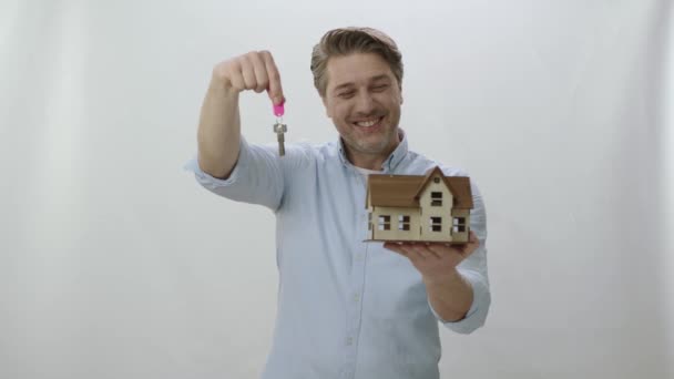 家や不動産を購入する 白い背景に隔離された彼の家にカメラキーを示す 彼が購入またはレンタルした新しい家の幸せな男のモックアップを保持します — ストック動画