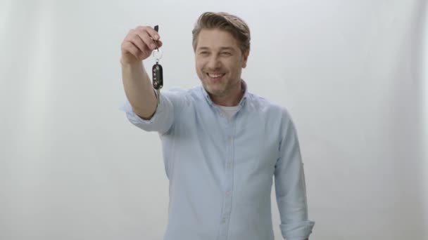 白の背景に隔離された彼の新しい車の鍵を示す興奮した若い男 カメラに彼の新しい車のキーを渡す幸せな若い男 車のローン 新しい車の購入の概念 — ストック動画