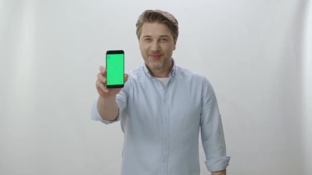 Милый Молодой Человек Показывает Смартфон Зеленым Экраном Стоя Над Изолированным — стоковое видео