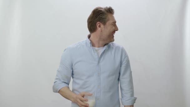 白いスタジオの背景に隔離された笑顔の白人男性 牛乳やバターミルクのカメラと飲料ガラスを見てカジュアルなスーツの若い男 ガラスの中の飲み物は非常に良いことを示す男 — ストック動画