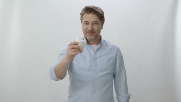 白い背景にミルクのガラスの若い男 男は牛乳を飲み 彼の両足を示す 健康だ カルシウムの力 白い背景にミルクを飲んだ後に二足歩行を示す若い男 — ストック動画