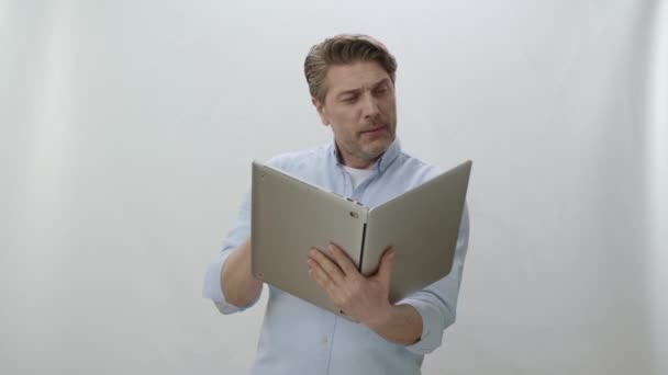 ノートパソコンを持っている男は白い背景に隔離された本のように 若い男はノートパソコンで本を読んでいるかのようにページを変更します 彼が見ているものに驚いて 将来の技術 — ストック動画