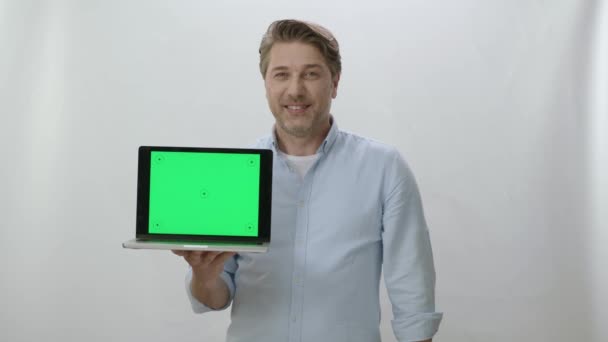 拥有绿色屏幕的笔记本电脑的快乐商人的肖像 在白色背景上工作的快乐商人展示了一切是完美的 你可以把任何你想要的东西放进电脑 — 图库视频影像
