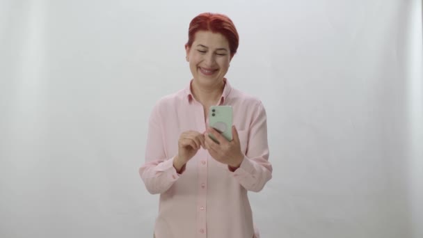 Punatukkainen Nainen Viettää Aikaa Internetissä Älypuhelimellaan Valkoisella Pohjalla Nainen Yllättynyt — kuvapankkivideo