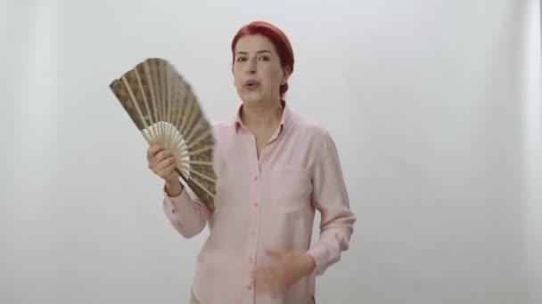 红头发女人用扇子冷却 被白色背景隔离的工作室 那女人手里拿着扇子在冷却 慢动作视频 — 图库视频影像