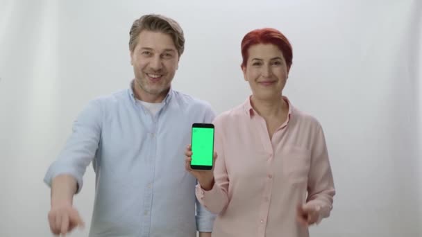 Pár Drží Smartphone Zelenou Obrazovkou Bílém Pozadí Pár Ukazujících Zelenou — Stock video