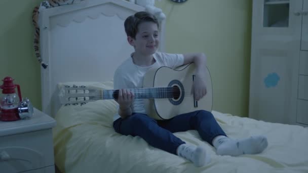 自分の部屋のベッドで一人でギターを弾くのが大好きな少年 ギターを弾く少年は音楽家になりたがっている 子供で楽器を演奏する概念 — ストック動画