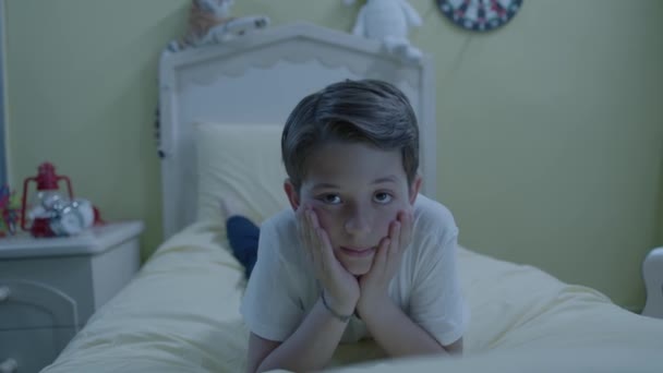 次の日の興奮のために 彼の頬に彼の手でベッドの上の彼のパジャマに横たわっている不幸な子供は眠ることができません — ストック動画