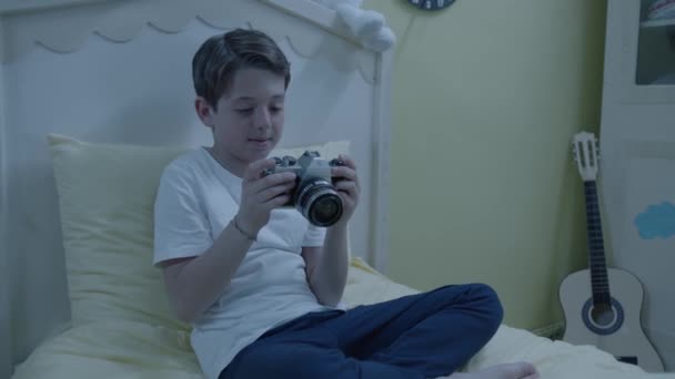Hermoso Niño Sentado Cama Pijama Examina Una Vieja Cámara Niño — Vídeo de stock