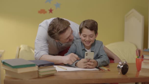Fiatal Apa Segít Gyerekének Házi Feladatot Hallgatni Okostelefonon Egy Fiatal — Stock videók